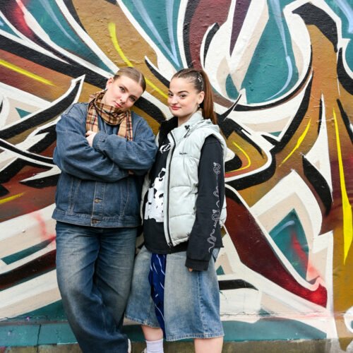 Two young women pose confidently in front of a large colourful graffiti mural in South East London