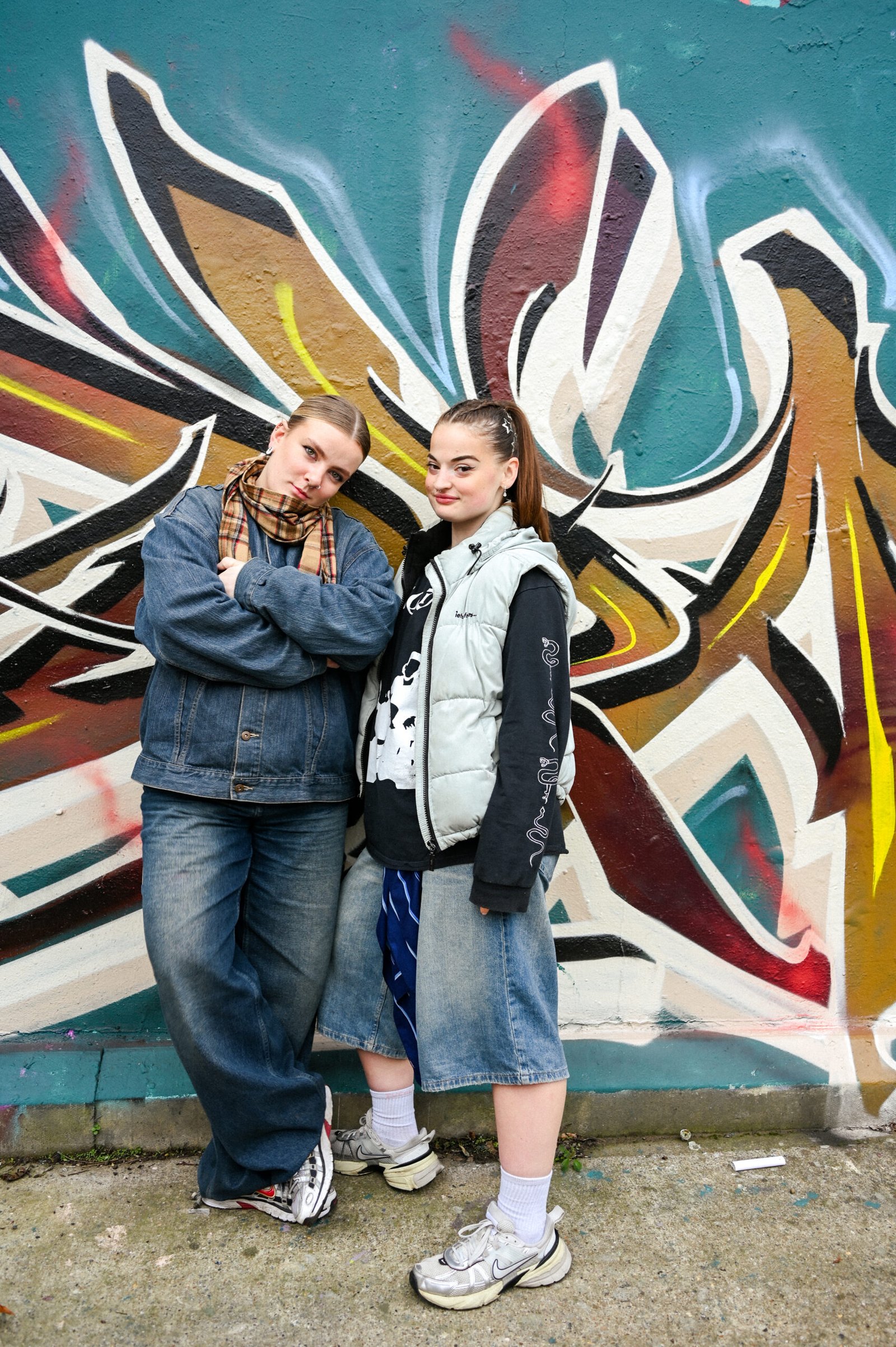 Two young women pose confidently in front of a large colourful graffiti mural in South East London